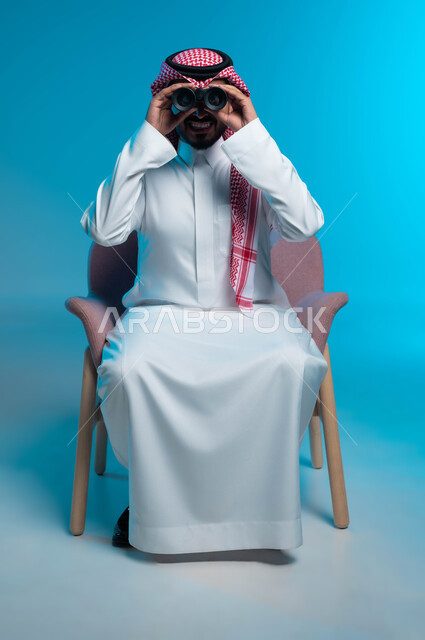Love of exploration and adventure, seeing distant things through a telescope, close-up portrait of a smiling Saudi Gulf Arab man wearing a traditional thobe and shemagh looking through binoculars, future planning for goals and ambitions, blue background