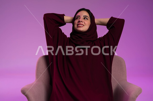 الشعور بالتعب و الخمول والحاجة إلى النوم, بورتريه مقرب لامرأة عربيه خليجيه سعوديه محجبه ترتدي العباءة الملونة تجلس على كرسي مريح تضع يديها وراء رأسها بتعابير التأمل والسرور، إيماءات الراحة والإسترخاء، النظر للأعلى إلى شيء ما، خلفية ملونه .