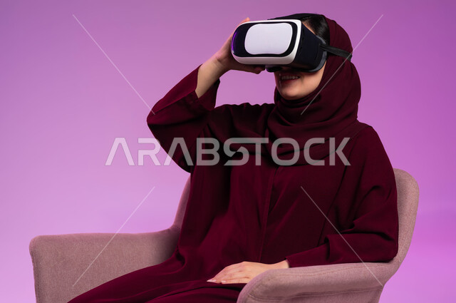 المتعة بمشاهدة أفلام الواقع الافتراضي ومحاكاة العالم الخيالي, بورتريه لشابة عربية خليجية سعودية ترتدي العباءة الملونة والحجاب ونظارة في آر ثلاثية الأبعاد تستمتع بالأنشطة الترفيهية, التطور التقني والتكنولوجي, خلفية وردية
