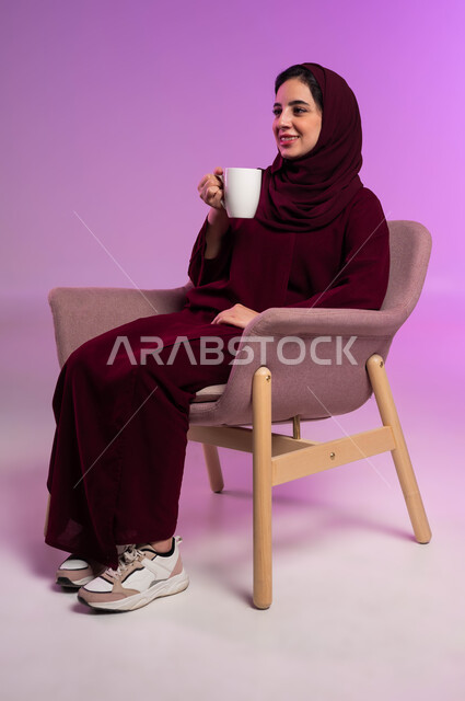 قضاء الوقت باحتساء المشروب المفضل, الحيوية والنشاط عن شرب الكافئيين, الاستمتاع بالمشروبات الساخنة والأعشاب الشتوية الدافئة, بورتريه لشابة عربية خليجية سعودية ترتدي العباءة الملونة والحجاب تستمتع بلحظات الهدوء والراحة,  خلفية وردية