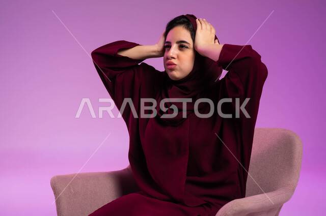 الاحساس بالصدمة والفشل, الشعور بالحزن لخسارة شيء ما, الحاجة إلى الهدوء والراحة, أوجاع وآلام الرأس, بورتريه مقرب لشابة عربية خليجية سعودية ترتدي العباءة الملونة والحجاب تضع يدها على رأسها, خلفية وردية