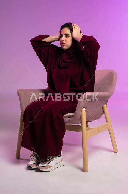 الشعور بالحزن لخسارة شيء ما, الاحساس بالصدمة والفشل, الحاجة إلى الهدوء والراحة, أوجاع وآلام الرأس, بورتريه لشابة عربية خليجية سعودية ترتدي العباءة الملونة والحجاب تضع يدها على رأسها, خلفية وردية