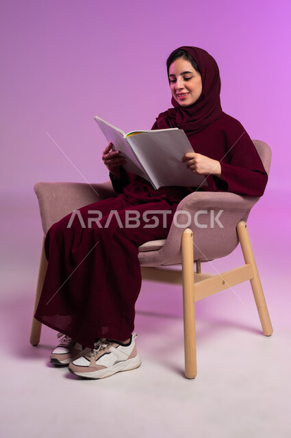 الاستمتاع بهواية القراءة والاستكشاف, قضاء وقت الفراغ بالتعلم والثقافة, مفهوم التثقيف والبحث العلمي, بورتريه لشابة عربية خليجية سعودية مبتسمة ترتدي العباءة الملونة والحجاب تقرأ الكتاب,  خلفية وردية