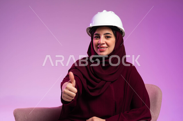 الجودة الفنية في تقنية التصميم والبناء، العمل في القطاع الهندسي، مفهوم الهندسة والانشاءات المعمارية, مهن ووظائف نسائية, بورتريه مقرب لمهندسة عربية خليجية سعودية ترتدي العباءة والخوذة البيضاء ترفع يدها بإيماءات الاعجاب والقبول, خلفية وردية