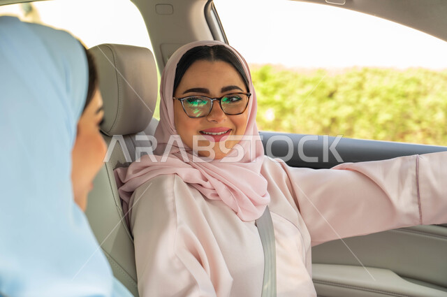 مفهوم الاعتماد على الذات، تجهيز وتحضير السيارة قبل القيادة في الطرق والشوارع العامة، صورة مقربة امرأتان عربيتان خليجيتان سعوديتان محجبتان تقومان تنظران لبعضهما بايماءات السرور، قضاء وقت ممتع في الخارج مع الاصدقاء، مفهوم حرية القيادة للنساء السعوديات