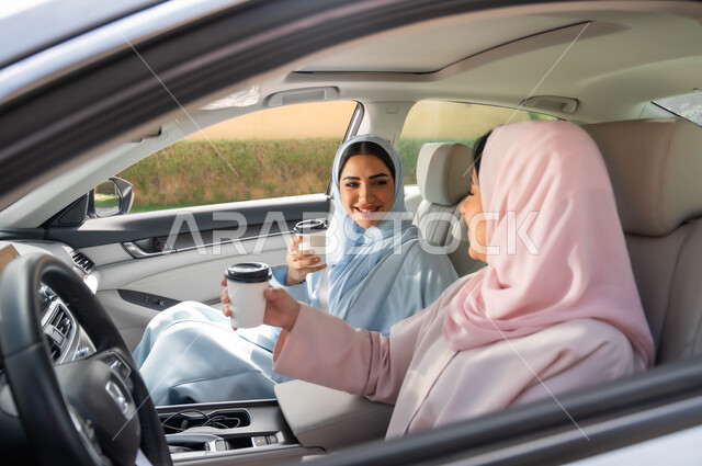 مفهوم الاستقلال و الاعتماد على النفس في وسائل النقل، تناول المشروبات الساخنه، التجول في شوارع المملكة ،قضاء أوقات ممتعه مع الأصدقاء، حرية القيادة للنساء السعوديات، صديقتان عربيتان خليجيتان سعوديتان محجبتان تجلسان في مقعد السيارة بإيماءات السرور