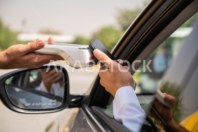 الدفع الالكتروني من خلال الهاتف المحمول عبر طلبات السيارة(الدرايف ثرو)، صورة مقربة ليد عربي خليجي سعودي يقوم باستخدام الأجهزة التقنية الحديثه ،دمج التكنولوجيا في الحياة اليومية لتوفير راحة أكبر للأفراد ،التنقل في شوارع المملكة
