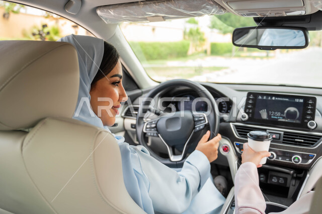 حرية القيادة للنساء السعوديات، صورة مقربة من الخلف لامرأة عربيه خليجية سعودية محجبه تجلس في مقعد السيارة برفقة صديقتها بإيماءات السرور، تناول المشروبات الساخنه، قضاء أوقات ممتعه مع الأصدقاء، مفهوم الاستقلال و الاعتماد على النفس في وسائل النقل والمواصلات