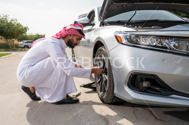 الفحص والتشييك على أجزاء السيارة, استخدام أدوات الصيانة اليدوية المناسبة، تعطل المركبة بشكل مفاجئ أثناء السير في الطريق، رجل عربي خليجي سعودي يرتدي الزي التقليدي السعودي يقوم بإصلاح بنشر العجلات