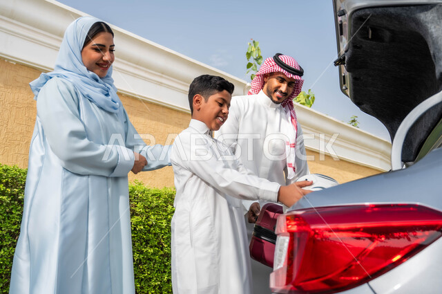 Preparing to travel with gestures of happiness and pleasure, preparing supplies for tourist entertainment tours and trips, putting things and bags in the car, a Saudi Arabian Gulf family preparing for an outing on the summer vacation, spending enjoyable family times abroad.