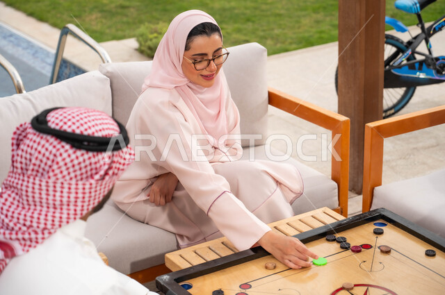 مفهوم الأسرة السعوديه المترابطة، الاستمتاع في العطلة الصيفية مع الأفراد في إحدى المنتجعات، عائلة عربية خليجية سعودية تقضي أوقات ممتعة في اللعب بلعبة الكيرم (البليارد) المسلية، ألعاب عائلية شعبية في المملكة.
