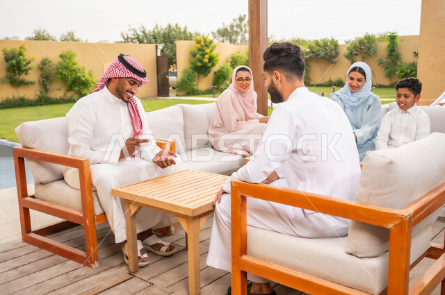 مفهوم التركيز والتحدي في لعب الشدة، قضاء وقت ممتع في ممارسة الأنشطة والألعاب المسلية، الاستمتاع والتسلية مع الأهل والأصدقاء في إحدى الشاليهات في العطلة الصيفية، رجلان عربيان خليجيان سعوديان يلعبان لعبة الورق بإيماءات السعادة والسرور