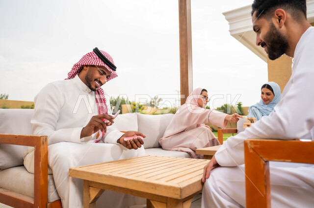 قضاء وقت ممتع في ممارسة الأنشطة والألعاب المسلية، مفهوم التركيز والتحدي في لعب الشدة، الاستمتاع والتسلية مع الأهل والأصدقاء في إحدى الشاليهات في العطلة الصيفية، رجلان عربيان خليجيان سعوديان يلعبان لعبة الورق بإيماءات السعادة والسرور