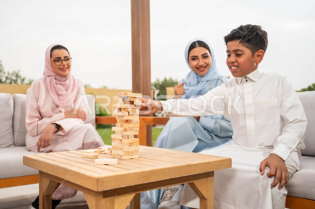 الاستمتاع والسرور بالأنشطة العائلية، قضاء أوقات ممتعة مع الأبناء في الإجازة الصيفية في إحدى المنتجعات، ألعاب مسلية لتنمية مهارات التفكير والذكاء عند الأطفال، عائلة عربية خليجية سعودية تلعب لعبة جينغا في الهواء الطلق، رص الألواح الخشبية.