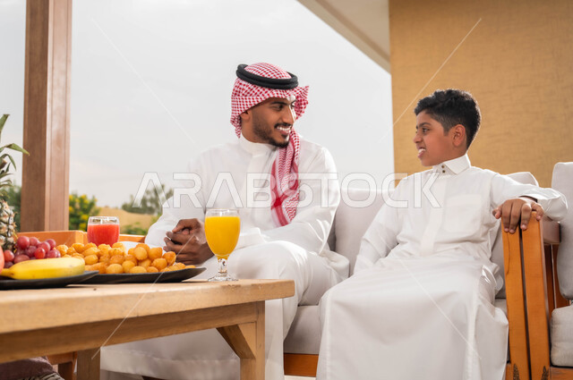 الاستمتاع بالأجواء الصيفيه والتنزه في الهواء الطلق، الاهتمام والاعتناء بالأبناء، أب عربي خليجي سعودي يرتدي الزي التقليدي برفقة ابنه في إحدى الشاليهات، الضحك والتسامر مع الأولاد، قضاء عطلة نهاية الاسبوع في الخارج