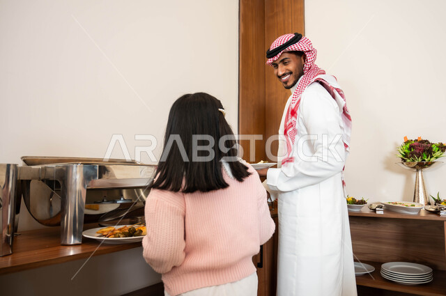 الاستمتاع مع الأبناء، اطباق متنوعه من المأكولات والمشروبات، مفهوم الخدمة الذاتية في المطاعم السعودية، رجل عربي خليجي سعودي مبتسم يرتدي الزي التقليدي يقوم بسكب الطعام من البوفيه في المطعم بصحبة ابنته