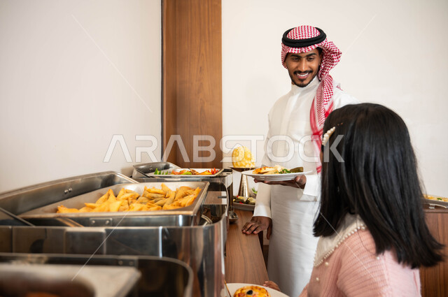 الاستمتاع مع الأبناء، اطباق متنوعه من المأكولات والمشروبات، مفهوم الخدمة الذاتية في المطاعم السعودية، رجل عربي خليجي سعودي مبتسم يرتدي الزي التقليدي يقوم بسكب الطعام من البوفيه في المطعم بصحبة ابنته