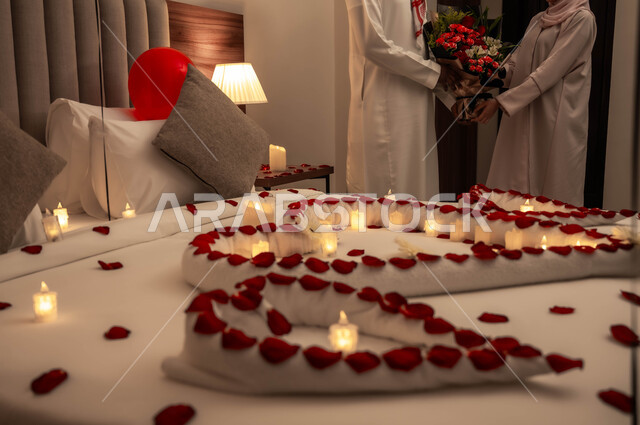 الاحتفال بذكرى الزواج، زوج عربي خليجي سعودي يقوم بتقديم باقة من الزهور لزوجته، سرير مزين بالشموع والورود الحمراء للاحتفال بيوم الفلنتاين، الاهتمام بالمناسبات الخاصة، تزيين غرفة النوم بطريقة رومانسية.