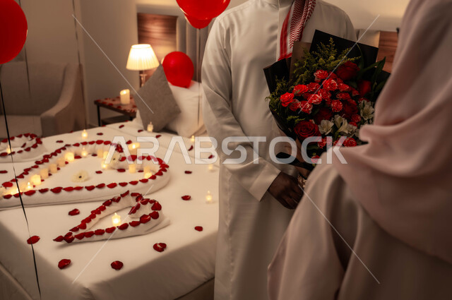 الاحتفال بذكرى الزواج، زوج عربي خليجي سعودي يقوم بتقديم باقة من الزهور لزوجته، سرير مزين بالشموع والورود الحمراء للاحتفال بيوم الفلنتاين، الاهتمام بالمناسبات الخاصة، تزيين غرفة النوم بطريقة رومانسية.