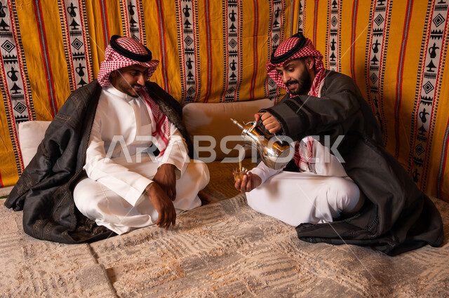 التسامر وتبادل الحديث في كشتة شعبية شبابية، مفهوم حسن الضيافه والاستقبال، صب القهوة من الدلة النحاسية، إيماءات البشاشة والترحيب، صديقان عربيان خليجيان سعوديان في جلسة بر وتخييم خارجية في الأجواء الشتوية