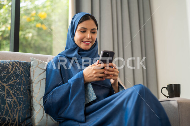 الدردشة والتحدث مع الأهل و الاصدقاء عبر الهاتف المحمول، ايماءات تدل على السعادة والاستمتاع بتصفح الانترنت من الهاتف الجوال، سيدة عربية سعودية خليجية تحمل بيدها الهاتف الخلوي