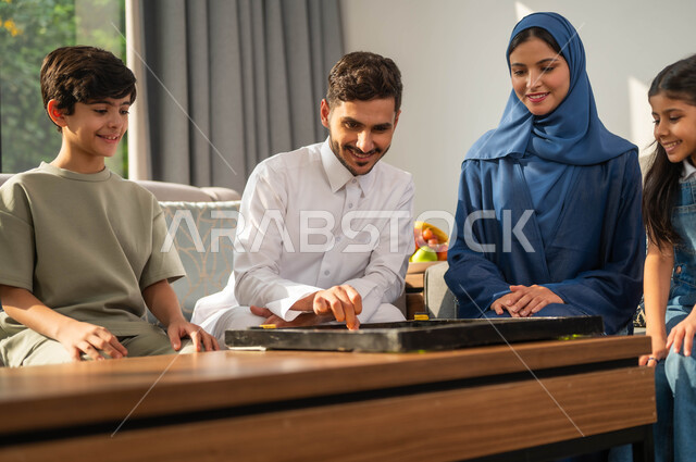 Spending enjoyable times with the children, the concept of challenge and competition, a family session in one of the luxurious chalets, an Arab father playing intelligence games with his son, a close-up photo of a Saudi Gulf Arab family, an atmosphere full of happiness and pleasure, family entertainment activities and events.
