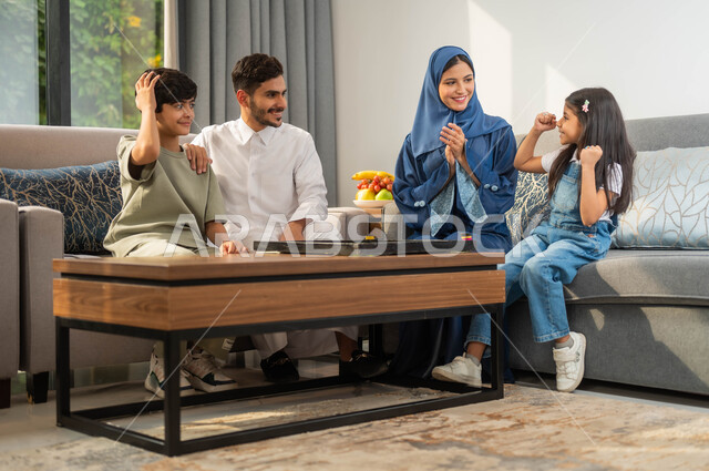 طفلة ترفع يديها بايماءات الفوز والنصر، جلسة عائلية في احدى الشاليهات الفاخرة، عائلة عربية خليجية سعودية تقضي وقت في اللعب، أجواء أسرية مليئة بالسعادة والسرور، مفهوم الترابط الاسري، قضاء أوقات ممتعة مع الأبناء، تبادل الاحاديث والدردشة بين أفراد الأسرة