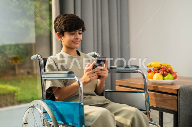 Gestures of integration and concentration, developing the capabilities of people with weak motor ability, using technology and modern techniques, chatting and communicating with family and friends, a close-up photo of a smiling Saudi Arabian Gulf child in a seat wearing a casual outfit using a mobile phone, the lifestyle of people of determination