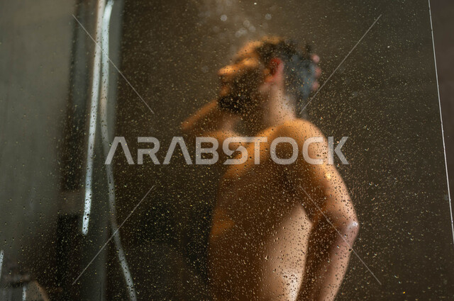 الاسترخاء والشعور بالراحة باستخدام الماء الساخن، مفهوم الاهتمام والعناية بالنظافة الشخصية، صورة مقربة لرجل عربي خليجي سعودي يقوم بالاستحمام داخل إحدى الشاليهات الفاخرة في السعودية