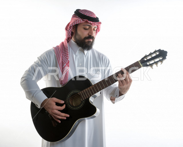بورتريه شاب سعودي عربي خليجي يعزف على  الجيتار( آلة وترية) ، شاب باللباس السعودية التقليديه بخلفية بيضاء ، آلة موسيقية ، مجال صوتي و فني