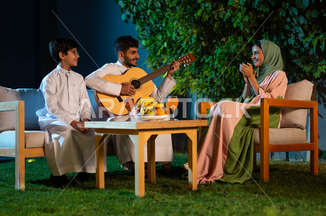 جلسة طربية مسائية في احدى الشاليهات الفاخرة، عائلة عربية خليجية سعودية تقضي وقت ممتع في الهواء الطلق، رجل عربي خليجي سعودي يقوم بالعزف على آلة الجيتارالوترية، مواهب وفنون موسيقية سعودية، اوقات عائلية مليئة بالسعادة والسرور، مفهوم الترابط الاسري