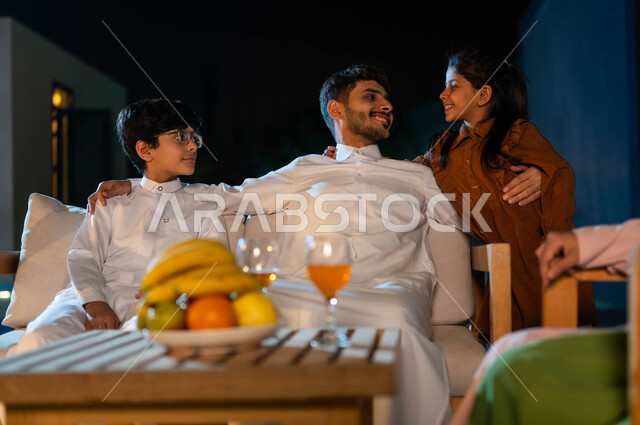 مفهوم الأبوة والاهتمام بالأولاد، قضاء أوقات عائلية ممتعة، ايماءات الفرح والسرور، عائلة عربية سعودية خليجية سعيدة في إحدى الشاليهات الفاخرة ، رعاية الأب لأبنائه والاستماع لهم