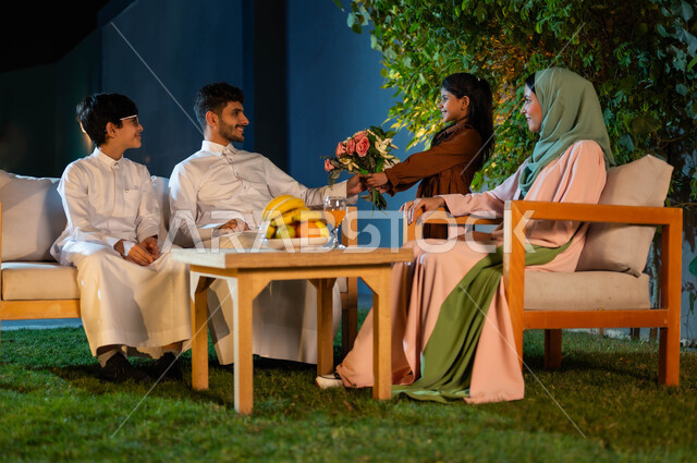 جلسة عائلية في المساء داخل إحدى الشاليهات الفاخرة في المملكة العربية السعودية، فلل وشقق سياحية، قضاء أوقات مسليه مع العائلة، مفهوم الترابط الأسري، ابنه تقدم باقة من الزهور لوالدها، إيماءات الفخر والأمتنان بالأب