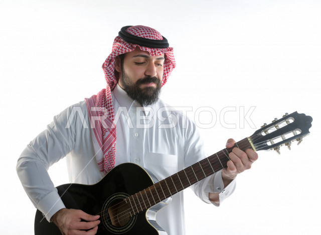 بورتريه شاب سعودي عربي خليجي يعزف على  الجيتار( آلة وترية) ، شاب باللباس السعودية التقليديه بخلفية بيضاء ، آلة موسيقية ، مجال صوتي و فني