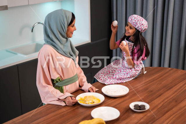 مشاركة البنات مهنة الطهي، إعداد وصفات شهية باستخدام البيض، امراة عربية سعودية خليجية تقوم بتحضير الطعام مع ابنتها في المطبخ، فتاه ترتدي زي الطبخ تساعد والدتها تجلس على الطاوله، قضاء أوقات سعيدة مع الأمهات، إعداد وصفات منزلية بسيطة