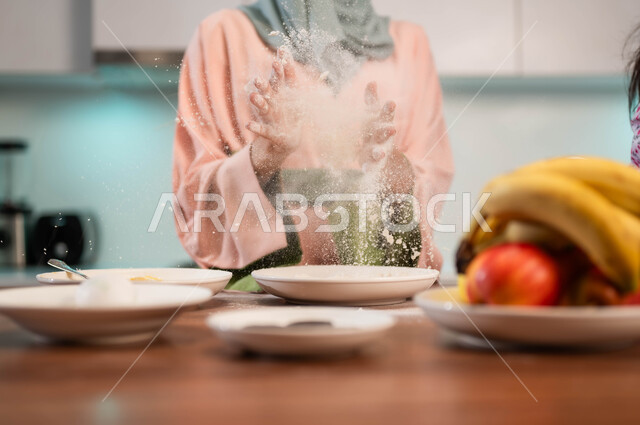 عمل وصفات شهيه بالدقيق والطحين الأبيض، سيدة ترتدي العباءة التقليدية الملونة في المطبخ، إعداد وتحضير العجين، أدوات وأطباق منزلية، صحن فاكهة طازجة، ايماءات يدين لامراة محجبة عربية خليجية سعودية تعد الطعام ، تحضير الوصفات الشهية والمغذية
