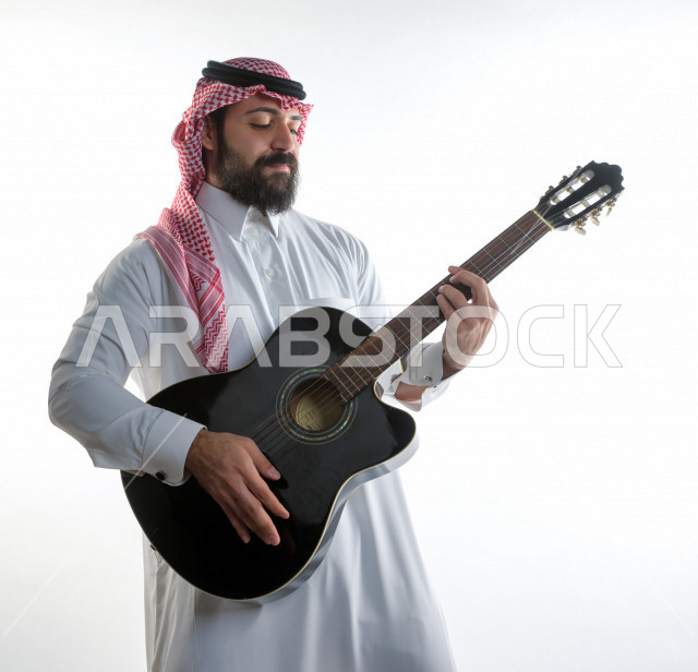 بورتريه شاب سعودي عربي خليجي يعزف على  الجيتار( آلة وترية) ، شاب باللباس السعودية التقليديه بخلفية بيضاء ، آلة موسيقية ، مجال صوتي و فني