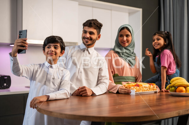 قضاء وقت ممتع برفقة العائلة ، توثيق اللحظات السعيدة بالتقاط صور السيلفي التذكارية عبر الجوال ، ايماءات الفرح والابتسامة والنظر إلى الهاتف المحمول , الإستعداد لأكل الكيكه المنزليه البيضاء، الاحتفال بالمناسبات السعيده في المنزل ، عائلة عربية سعودية خليجية