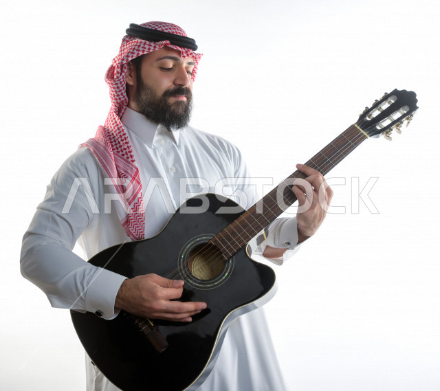بورتريه شاب سعودي عربي خليجي يعزف على  الجيتار( آلة وترية) ، شاب باللباس السعودية التقليديه بخلفية بيضاء ، آلة موسيقية ، مجال صوتي و فني
