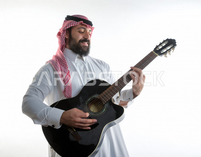 بورتريه شاب سعودي عربي خليجي يعزف على  الجيتار( آلة وترية) ، شاب باللباس السعودية التقليديه بخلفية بيضاء ، آلة موسيقية ، مجال صوتي و فني