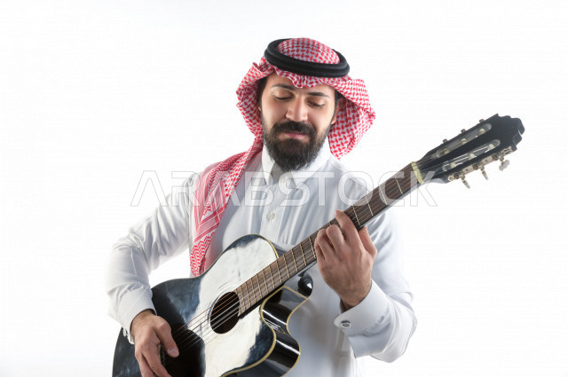 بورتريه شاب سعودي عربي خليجي يعزف على  الجيتار( آلة وترية) ، شاب باللباس السعودية التقليديه بخلفية بيضاء ، آلة موسيقية ، مجال صوتي و فني
