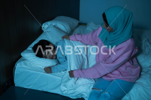 A Saudi Arabian Gulf mother checks on her child before bed, the concept of care and concern for children, the benefits of early sleep, a child sleeping in a fresh and comfortable bed on a soft white pillow, relaxing and enjoying the quiet atmosphere, following a healthy lifestyle