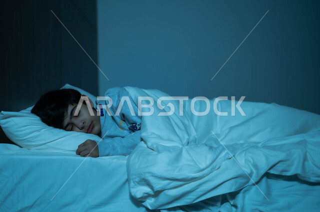 The concept of relaxing and enjoying the quiet atmosphere, following a healthy lifestyle, the benefits of early sleep, a Saudi Arabian Gulf child sleeping in a fresh and comfortable bed on a soft white pillow, feeling comfortable and reassured