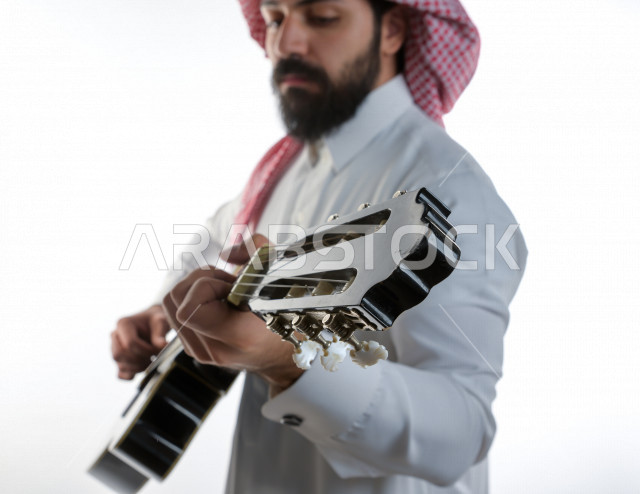 بورتريه شاب سعودي عربي خليجي يعزف على  الجيتار( آلة وترية) ، شاب باللباس السعودية التقليديه بخلفية بيضاء ، آلة موسيقية ، مجال صوتي و فني