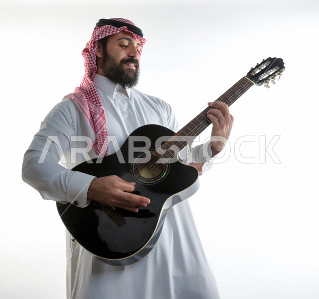 بورتريه شاب سعودي عربي خليجي يعزف على  الجيتار( آلة وترية) ، شاب باللباس السعودية التقليديه بخلفية بيضاء ، آلة موسيقية ، مجال صوتي و فني