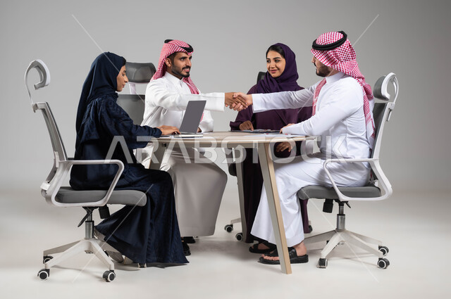 اتفاقيات وصفقات عمل جديدة، إيماءات التهنئة والنجاح في تحقيق اهداف الشركة, مفهوم روح الفريق والإنجاز الجماعي,  بورتريه مقرب لموظف عربي سعودي خليجي يقوم بمصافحة زميله, استخدام التكنولوجيا والتقنيات الحديثة، خلفية رمادية