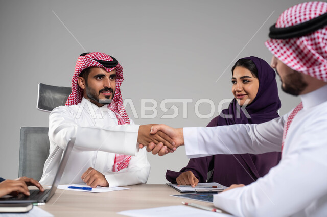 إيماءات التهنئة والنجاح في تحقيق اهداف الشركة, توفير بيئة عمل مريحة، مفهوم روح الفريق والإنجاز الجماعي, تطوير الاستراتيجيات و الأعمال,  بورتريه مقرب لموظف عربي سعودي خليجي يقوم بمصافحة زميله, خلفية رمادية