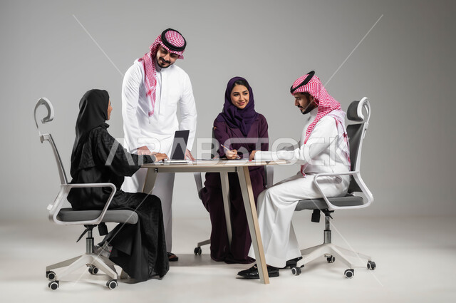 The concept of cooperation and teamwork, dialogues and discussions within the team, providing a suitable work environment, a close-up portrait of Saudi-Gulf Arab employees in a meeting, success and achieving goals, using modern devices and technologies in completing office work, gray background