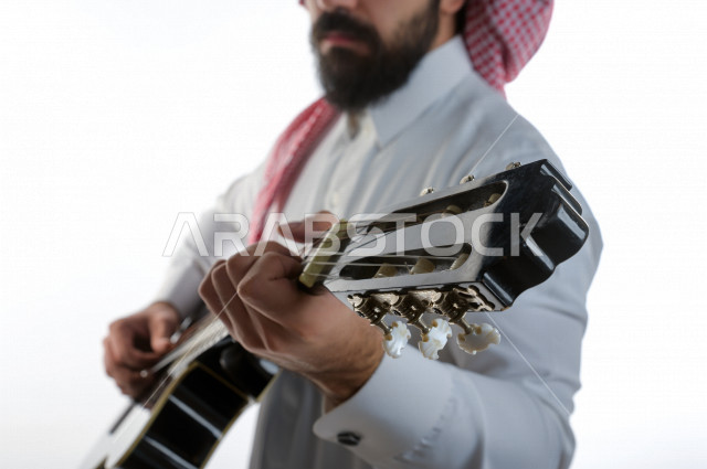 بورتريه شاب سعودي عربي خليجي يعزف على  الجيتار( آلة وترية) ، شاب باللباس السعودية التقليديه بخلفية بيضاء ، آلة موسيقية ، مجال صوتي و فني
