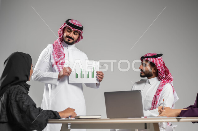 شرح المخططات والرسوم البيانية، الحوارات والنقاشات بين الزملاء، ، بورتريه لموظف عربي خليجي سعودي يرتدي الشماغ والثوب التقليدي يحمل بيده أوراق, تطوير الخطط والاستراتيجيات، استخدام التقنيات الالكترونية الحديثة،  خلفية رمادية